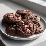 A plate of fudgy double chocolate peppermint cookies topped with chocolate chips and crushed candy canes.