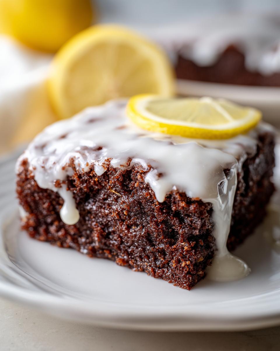 Close-up of a fudgy, dark square of Lemon Brownies topped with thick white glaze and a lemon slice.