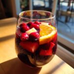 A condensation-covered glass filled with rich red holiday sangria, garnished with cranberries, orange slices, and apple chunks.
