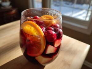 Close-up of a glass filled with rich red holiday sangria, loaded with cranberries, orange slices, and apple chunks.