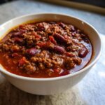 Close-up of a white bowl filled with rich, meaty chili featuring kidney beans and a thick, savory sauce.