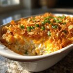 A close-up of a baked hot chicken salad casserole topped with melted cheese, crushed chips, and green onions.