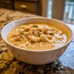 A close-up of a white bowl filled with creamy instant pot white chicken chili, showing shredded chicken and white beans.