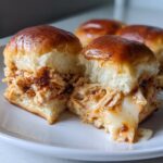 Close-up of a bbq chicken sliders bun cut in half, showing shredded chicken coated in sauce and melted cheese oozing out.