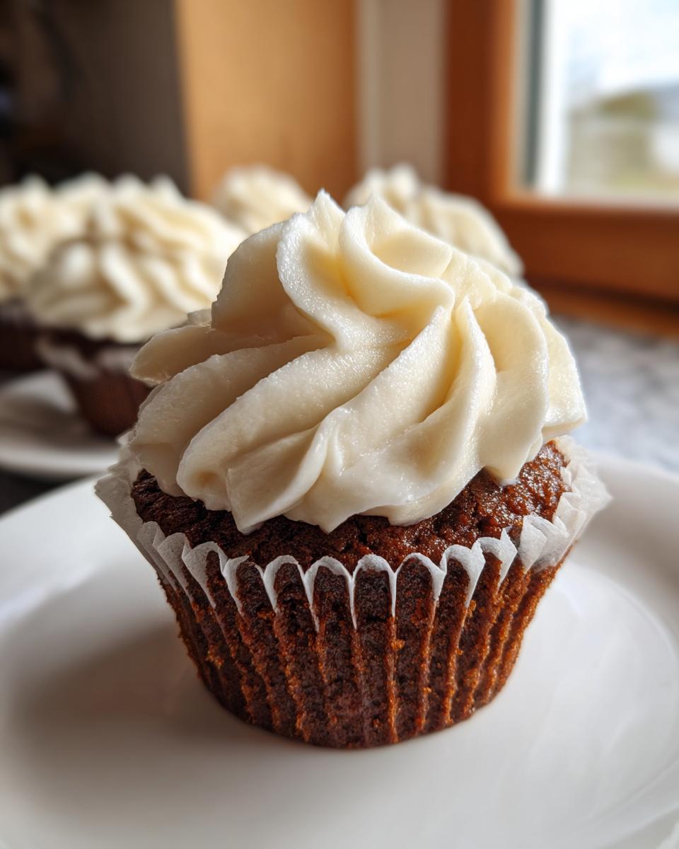 Close-up of a moist gingerbread cupcake topped with a swirl of creamy white frosting.