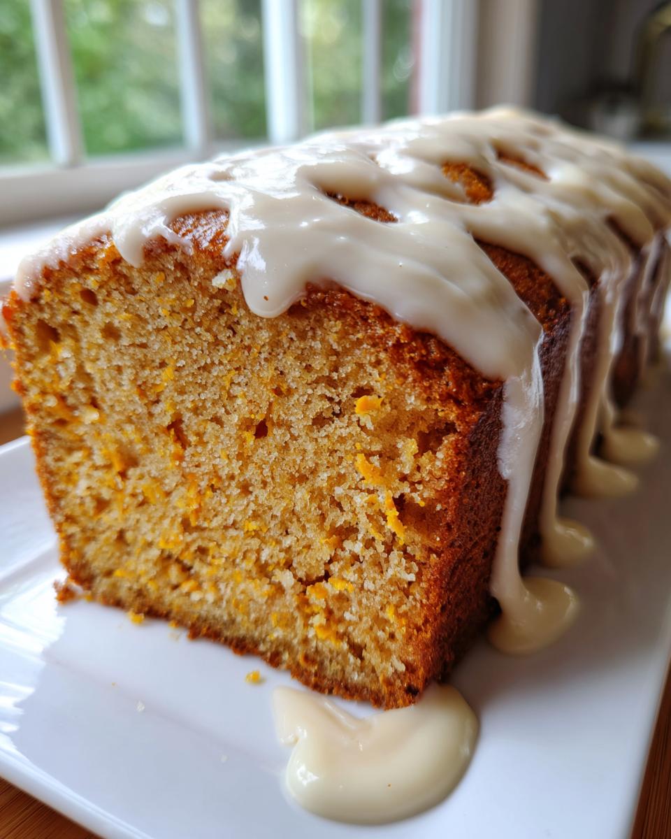 A close-up of a slice of moist sweet potato pound cake topped with a thick, dripping vanilla glaze.
