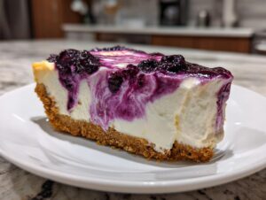 A close-up of a creamy slice of no bake blueberry cheesecake with a graham cracker crust and blueberry topping swirl.