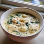 A close-up of a white bowl filled with creamy Olive Garden Chicken Gnocchi Soup, featuring soft gnocchi, shredded chicken, and spinach.