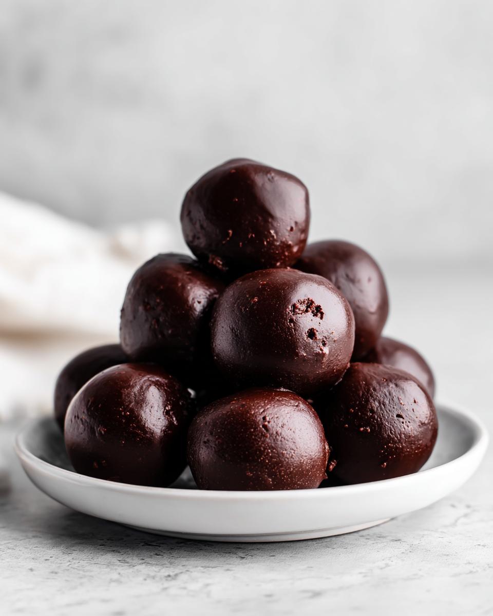 A close-up stack of dark, rich chocolate Oreo balls piled high on a small white saucer.