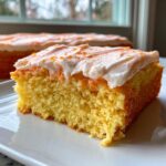 Close-up of a moist slice of Creamsicle Cake with thick white frosting and orange zest sprinkles.