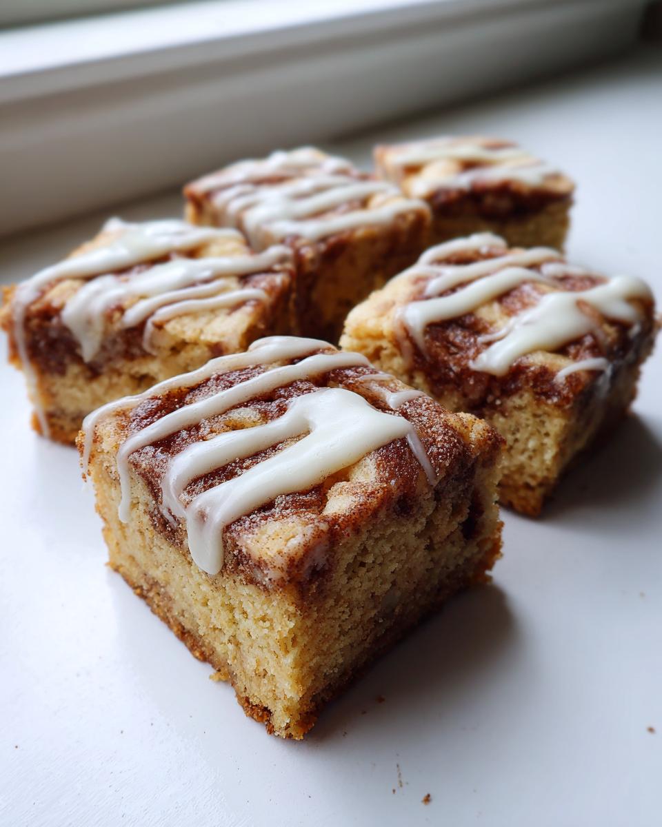 Several squares of moist snickerdoodle blondies with cinnamon swirl and vanilla icing drizzle.