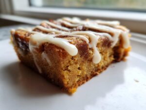 A single square of moist snickerdoodle blondies topped with a swirl of white icing, sitting on a white plate.