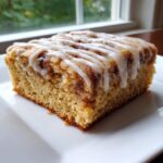 A square slice of moist snickerdoodle blondies featuring a cinnamon swirl and topped with a white vanilla icing drizzle.