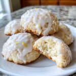 A stack of soft ricotta cookies topped with white glaze and lemon zest, one cookie is broken open showing the texture.