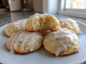 A stack of soft ricotta cookies drizzled with white lemon glaze, one cookie broken open showing the texture.