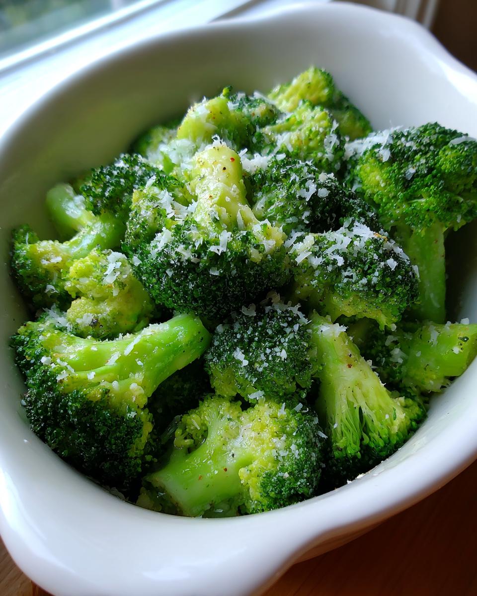 Close-up of bright green steamed broccoli florets topped with grated Parmesan cheese and pepper.