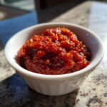 A close-up of thick, vibrant red tomato sauce with visible texture, served in a small white bowl.