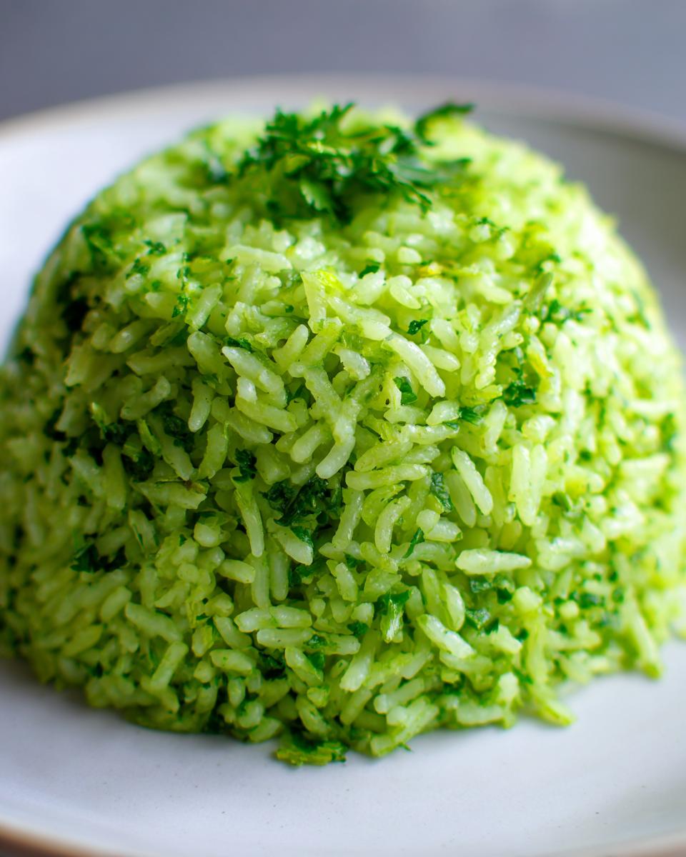 A close-up of a perfectly molded mound of bright green cilantro lime rice, garnished with fresh herbs.