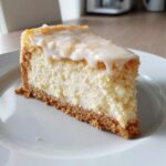 A perfect slice of creamy white chocolate cheesecake with a graham cracker crust and white chocolate glaze drizzled on top.